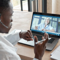 Black male doctor consulting senior patient by telemedicine online video call.